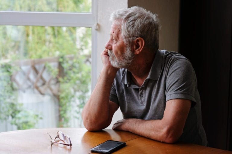 Senior retired man sitting at home alone looking out the window