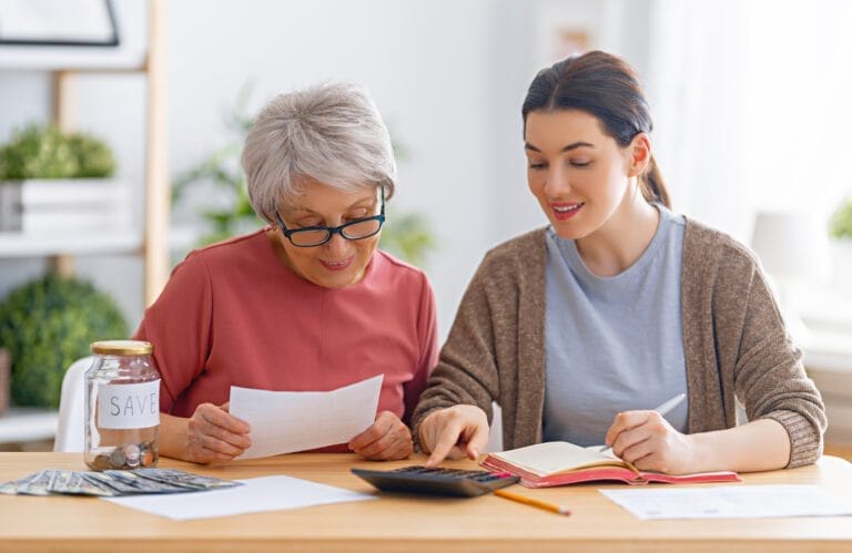Two women, sitting on the sofa with a paper receipt, are calculating expenses, managing the family budget.