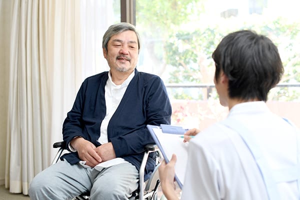 Asian adult man in a wheelchair talking with a caregiver