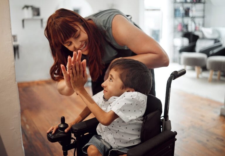 Caregiver high fiving a young boy in a wheelchair