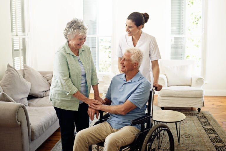 Smiling, older man in wheelchair with wife and nurse at hospital lobby