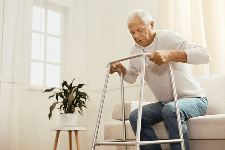 Older adult man rising from a sofa using a walker